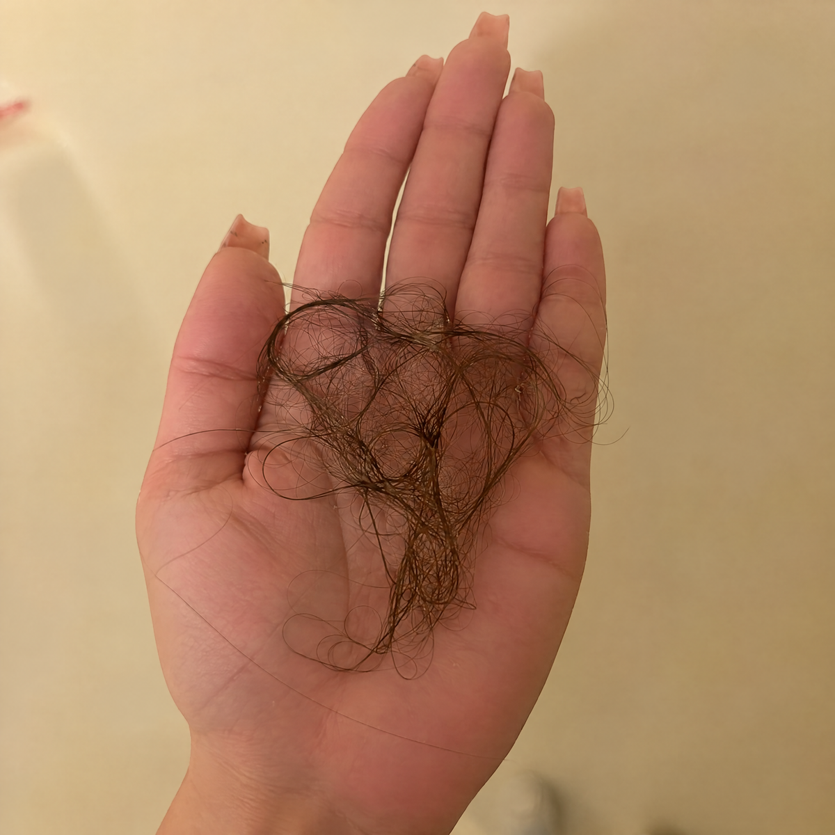 A hand over a shower drain with strands of shed hair on bathroom tiles